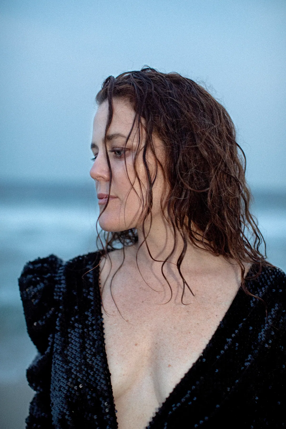 iskwē in a black sequined dress by the ocean, wet hair, looking away